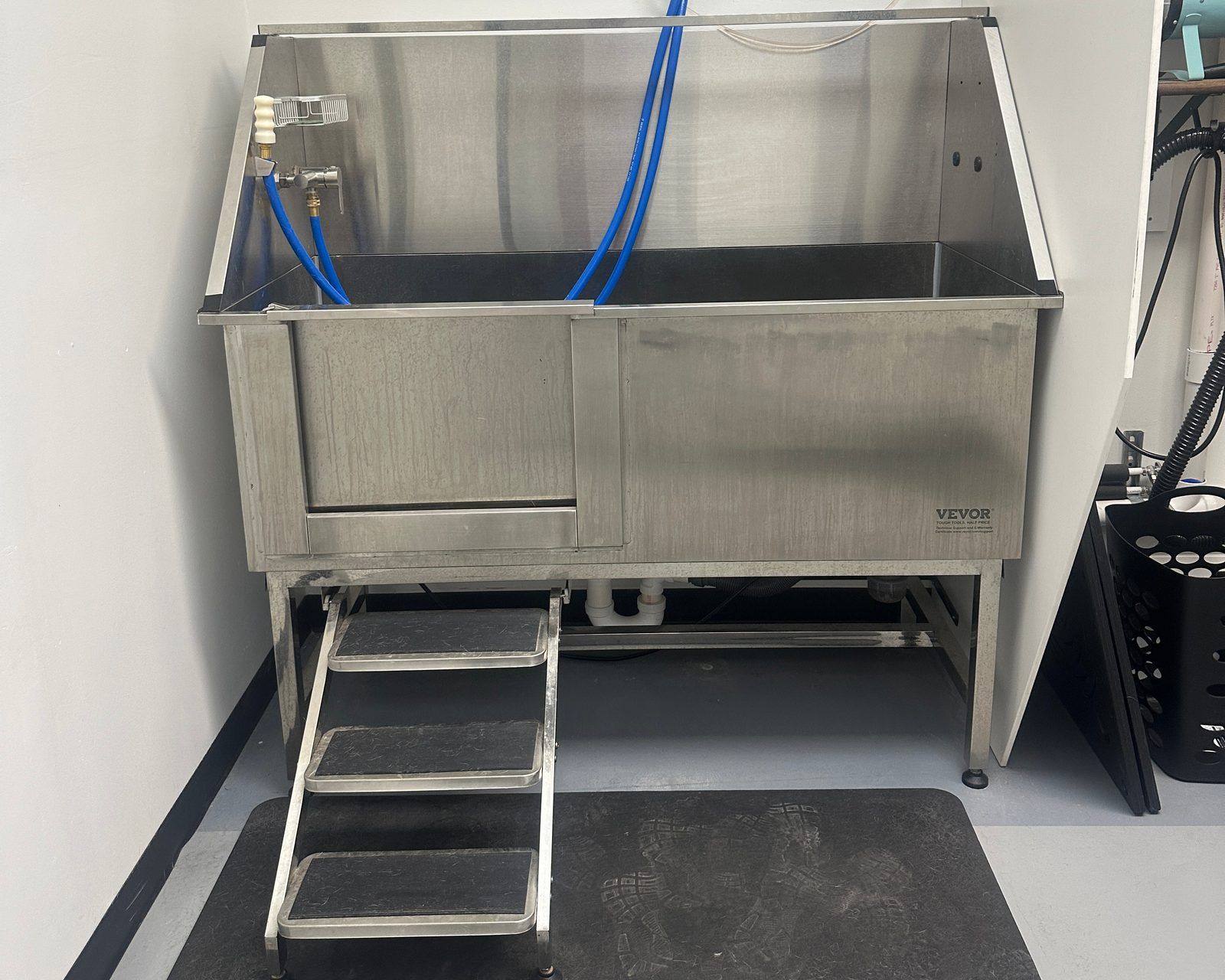 A Dapper Doodle self-wash station: a raised stainless steel tub with a step ramp up to it, sprayer hoses, and a rubber floor mat